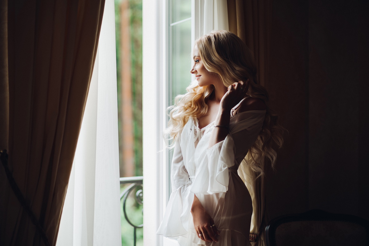 Gorgeous bride standing near balcony and looking in big window.